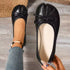 Top view of black bow flats with one shoe worn and one held
