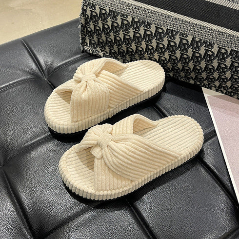 Beige fleece bow slide slippers resting on a dark seat