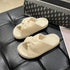 Beige fleece bow slide slippers resting on a dark seat