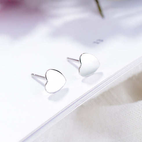 Front view of polished sterling silver heart studs with posts resting on a white card