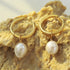 Close-up of gold-plated freshwater pearl hoops on a textured surface