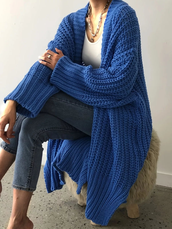 Blue chunky longline cardigan worn open over a white top, seated view