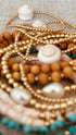 Conch-shell bracelet and gold-filled beads in a jewelry stack with decorative text