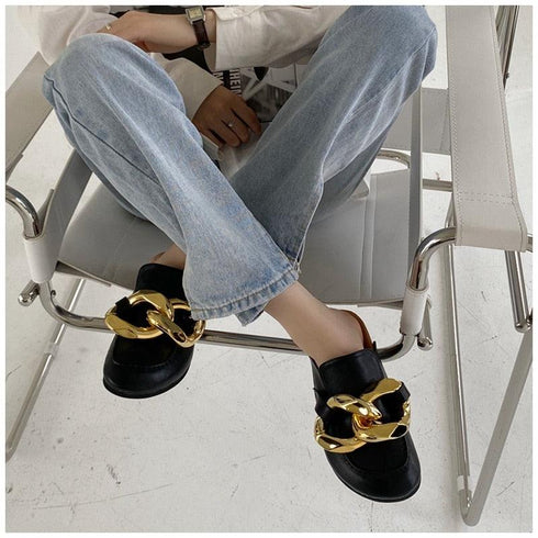 Black chain-detail mules worn while seated in blue jeans