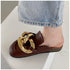 Close side view of a brown chain mule worn with cropped blue jeans