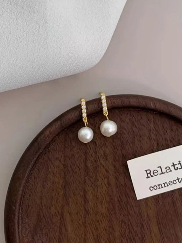 Synthetic Pearl Drop Earrings: Small gold-tone hoop earrings with white bead drops on wooden tray