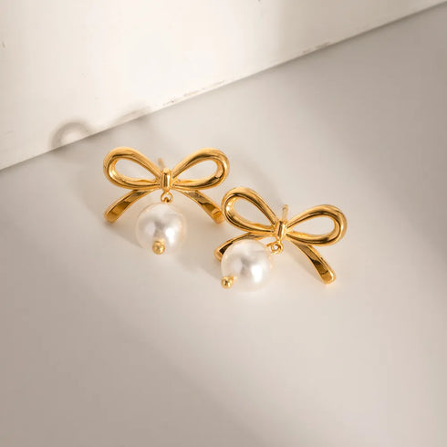 Gold-Tone Bow Earrings with Synthetic Pearls: Gold-tone bow earrings with white bead drops, angled flat lay