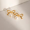 Gold-Tone Bow Earrings with Synthetic Pearls: Gold-tone bow earrings with white bead drops, angled flat lay