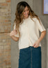 Zadie short-sleeve ivory cardigan paired with a dark denim skirt beside a brick wall