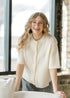 Zadie ivory ribbed short-sleeve cardigan worn buttoned while leaning beside a window