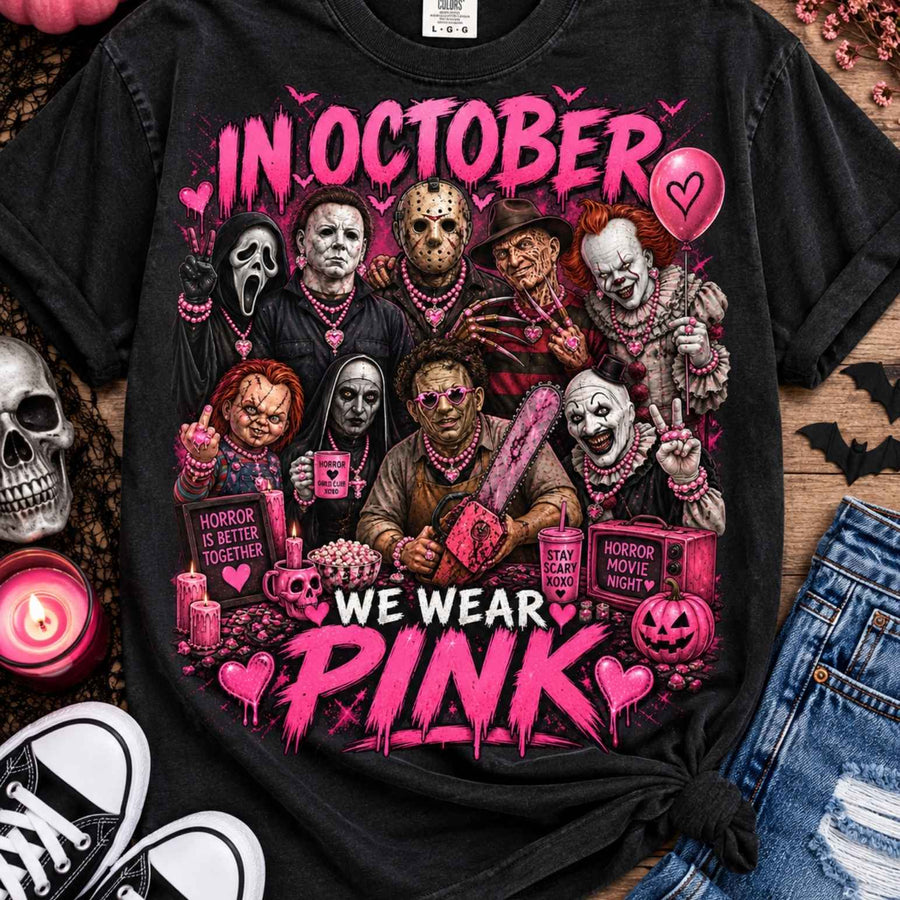 In October We Wear Pink Horror Icons Halloween Graphic T-Shirt: Black horror-character collage tee with In October We Wear Pink lettering, flat lay